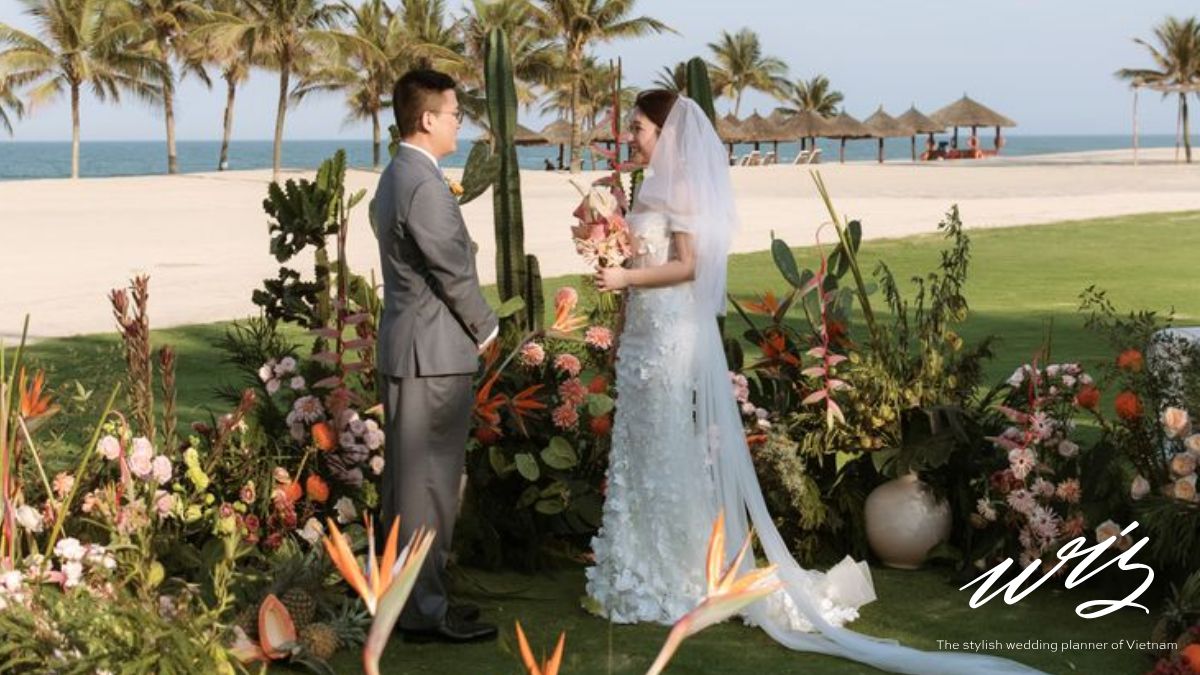 A bride and groom standing at a beachside altar with tropical floral decor, illustrating what is included in a Vietnam destination wedding cost