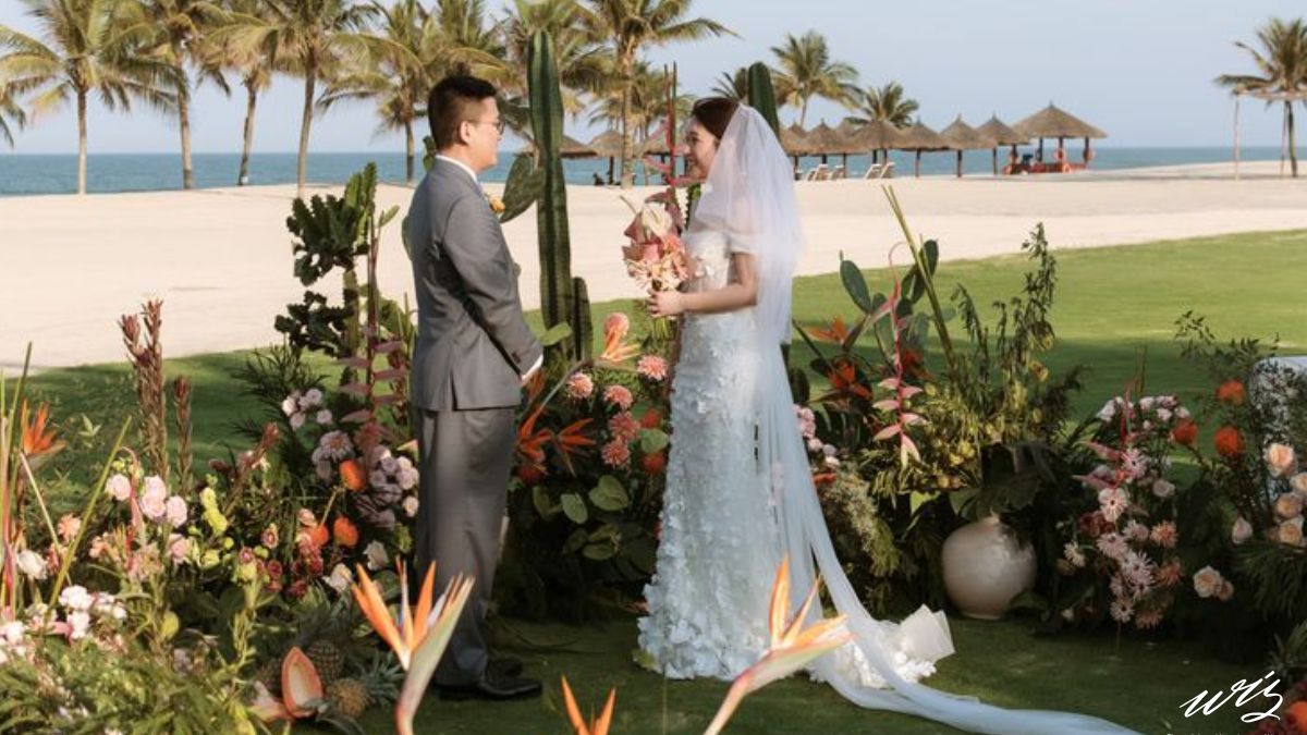 A bride and groom standing at a beachside altar with tropical floral decor, illustrating what is included in a Vietnam destination wedding cost